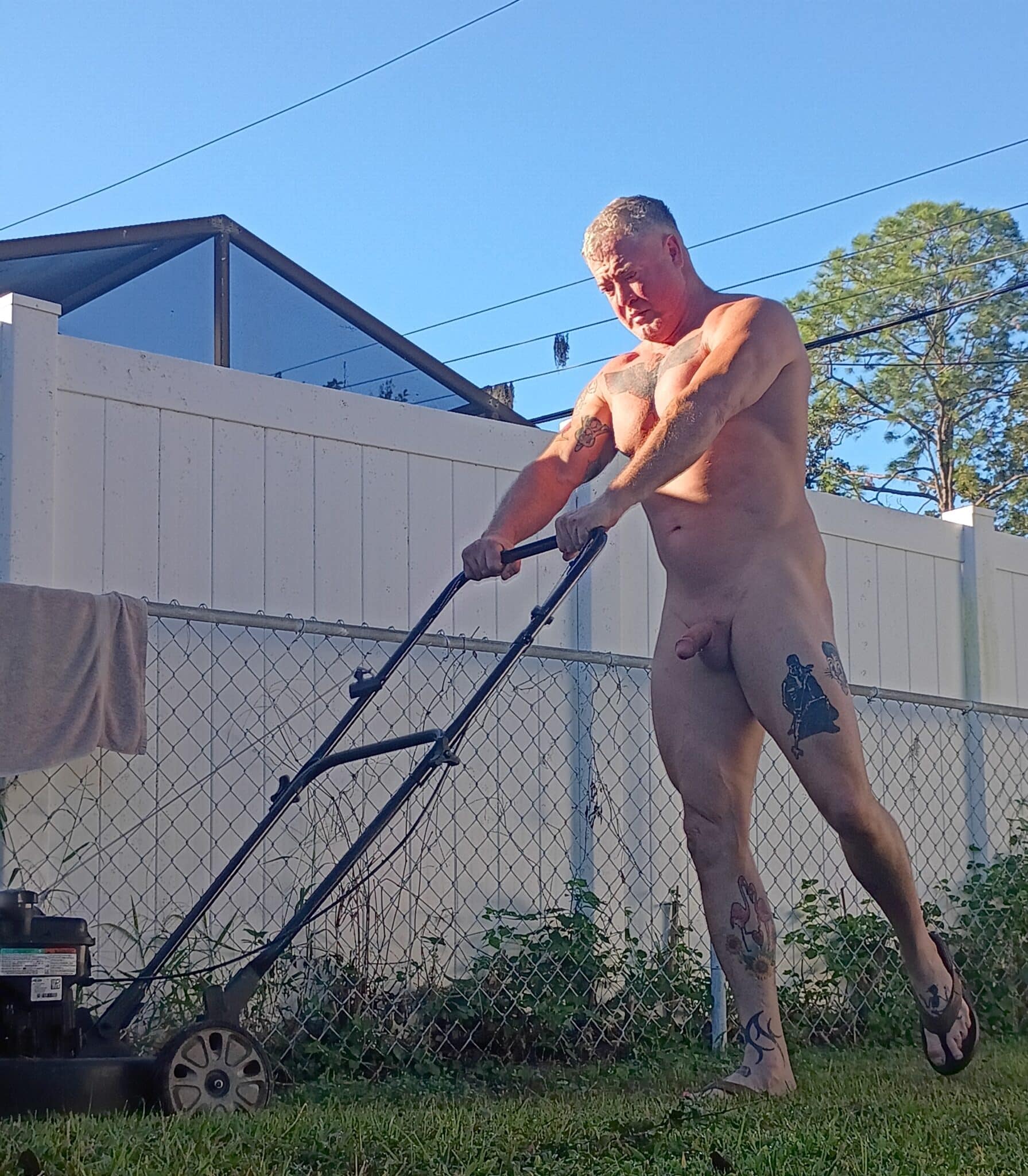 Amateur: Amateur Nudity: Mowing the Yard in the Nude A muscular man mows the lawn nude, showcasing his athletic build and tattoos, with a focus on his semi-hard cock and shaved balls.